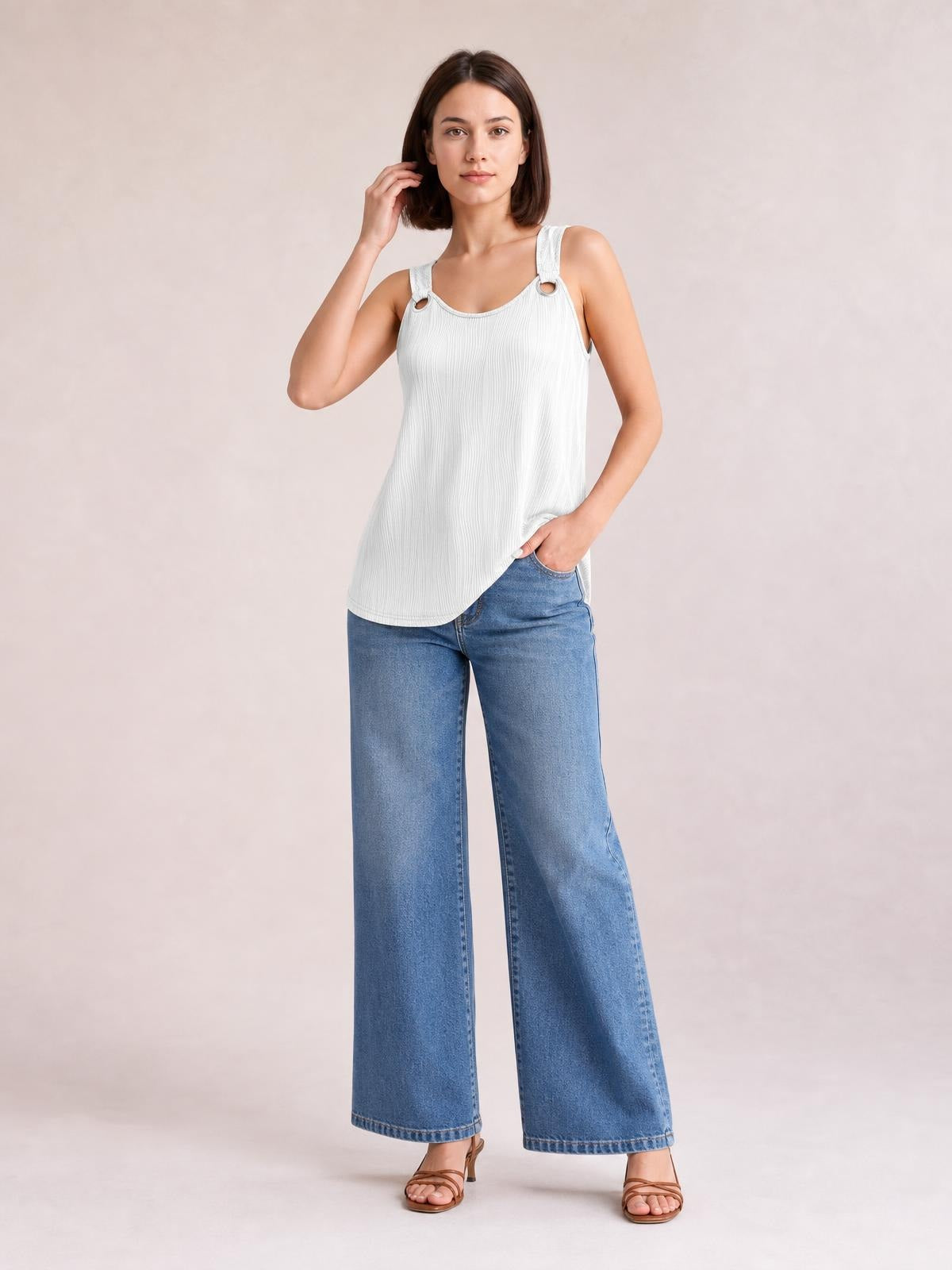 Model poses in a white round neck wide strap tank with a relaxed, slightly loose silhouette, textured vertical detailing, and rounded hem.