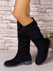 Model wearing black round-toe block heel boots with slouchy mid-calf shafts, side-by-side in a crossed-leg pose.