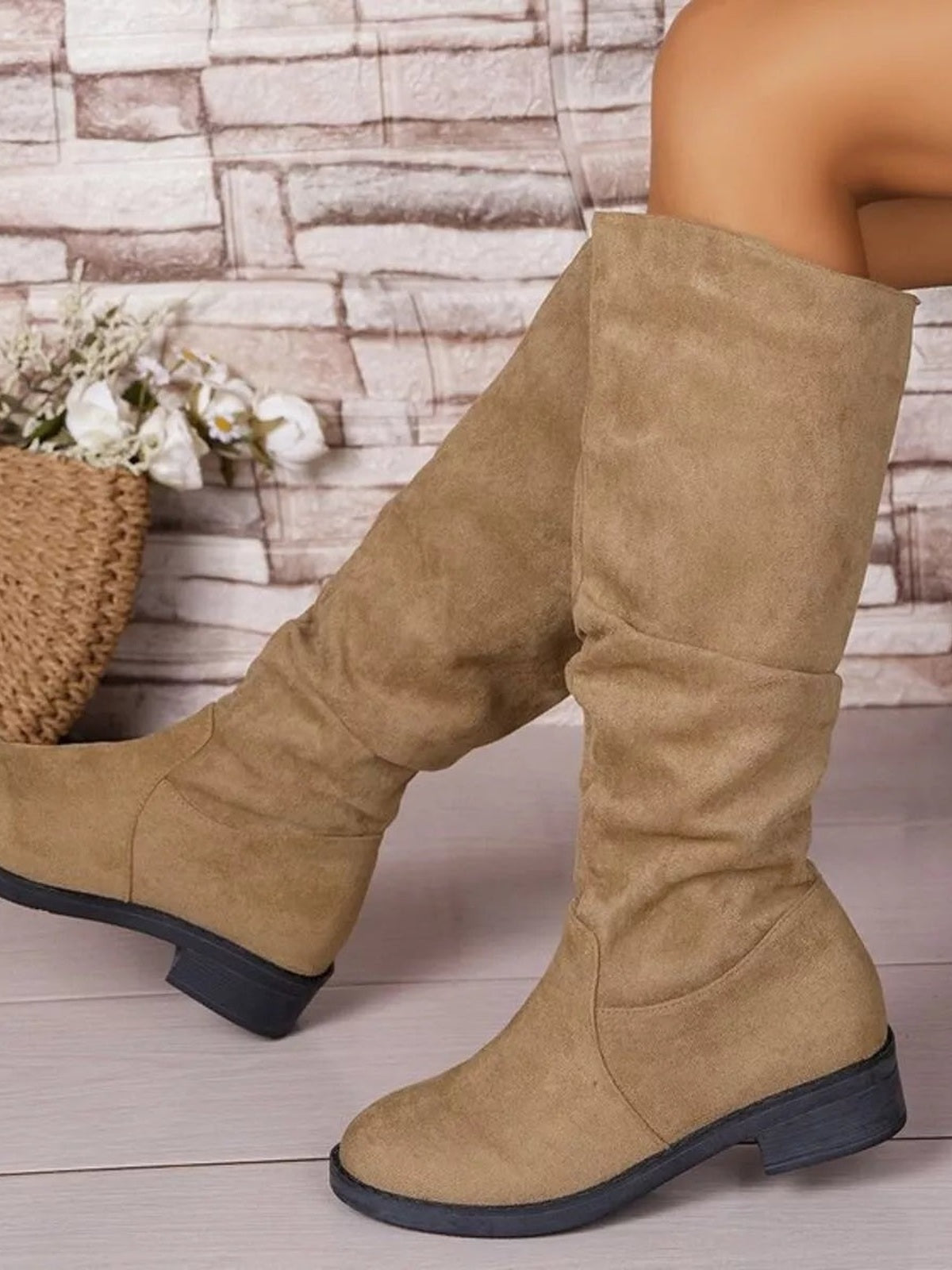 Model wearing tan round-toe block heel boots with a tall slouchy shaft, stitched panel construction, and low mid-height rubber heels.