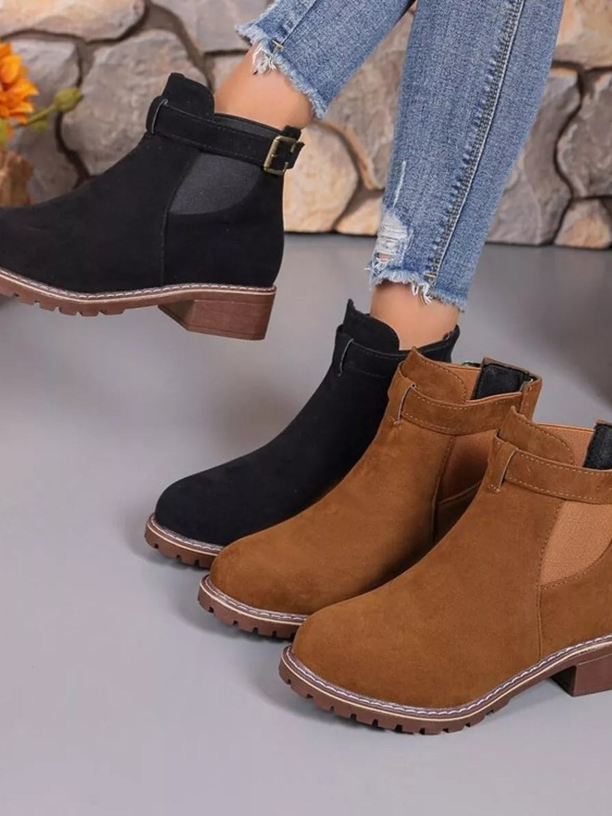 A model lifts one foot in black round-toe block-heel ankle boots, while brown versions show buckle straps, stitched trim, and lugged rubber soles.