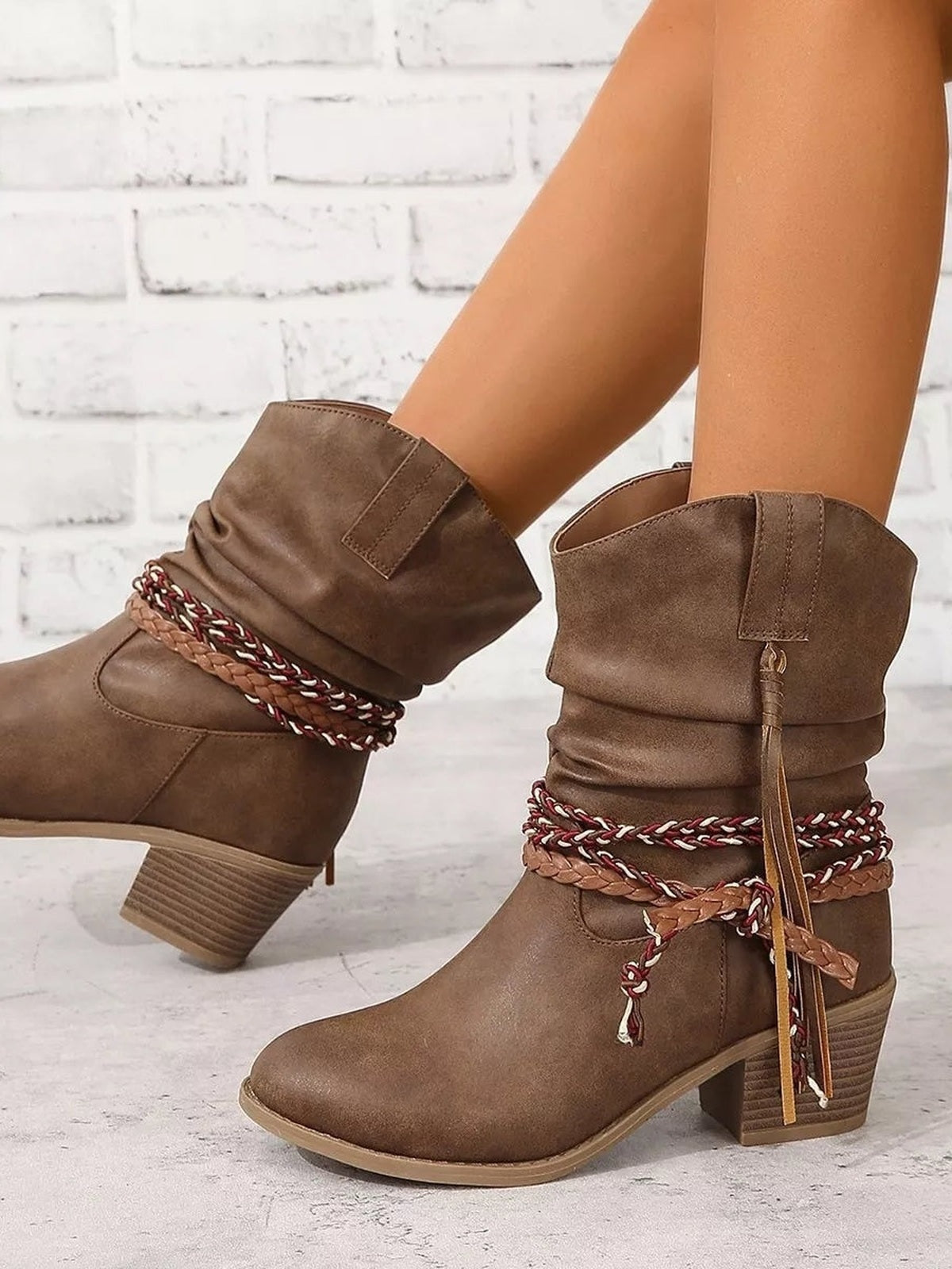 A model poses in brown PU leather round-toe ankle boots with slouchy cuffs, braided wrap accents, and low block heels.
