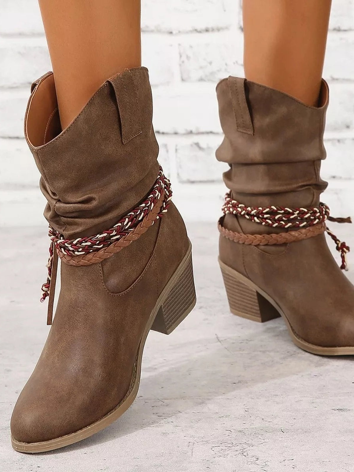 A model wears taupe PU leather boots with round toes, slouchy shafts, braided ankle straps, and low block heels in a relaxed silhouette.