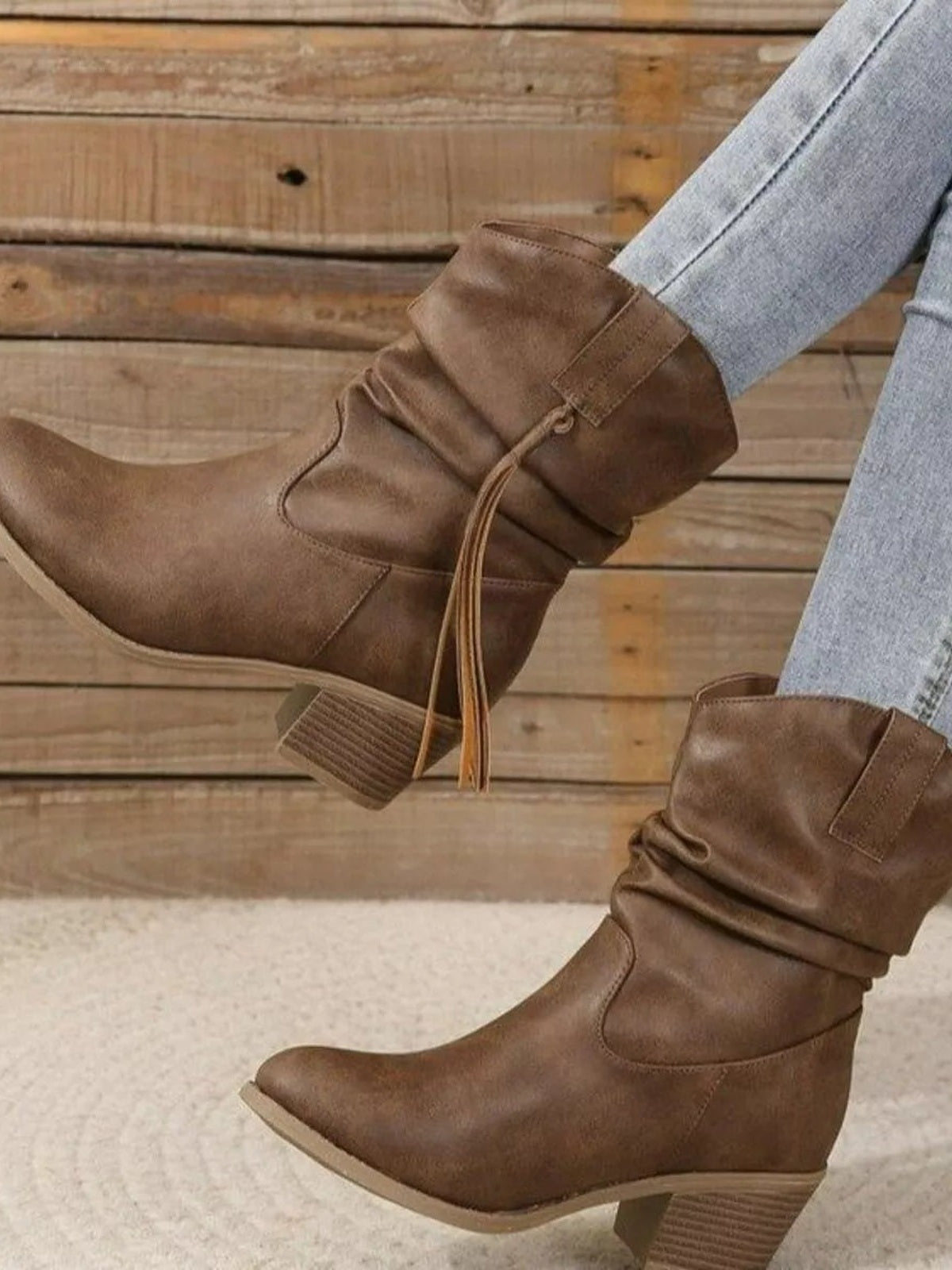 A model wears brown PU leather round toe block heel boots with slouchy shafts, stitched panels, and low textured heels over light gray jeans.