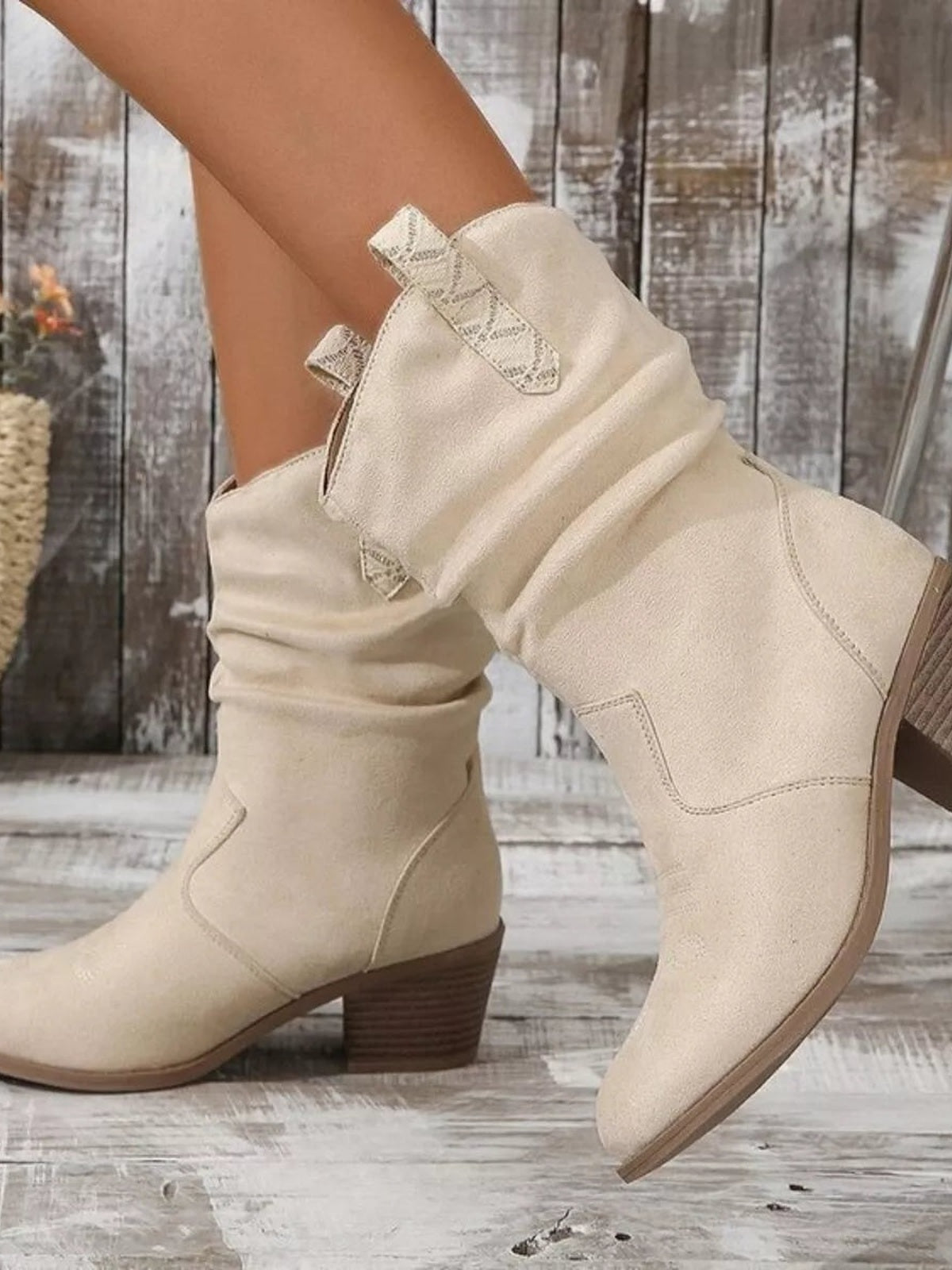 A model poses in cream round-toe block-heel boots with stitched panels, pull tabs, and low stacked heels in a structured silhouette.