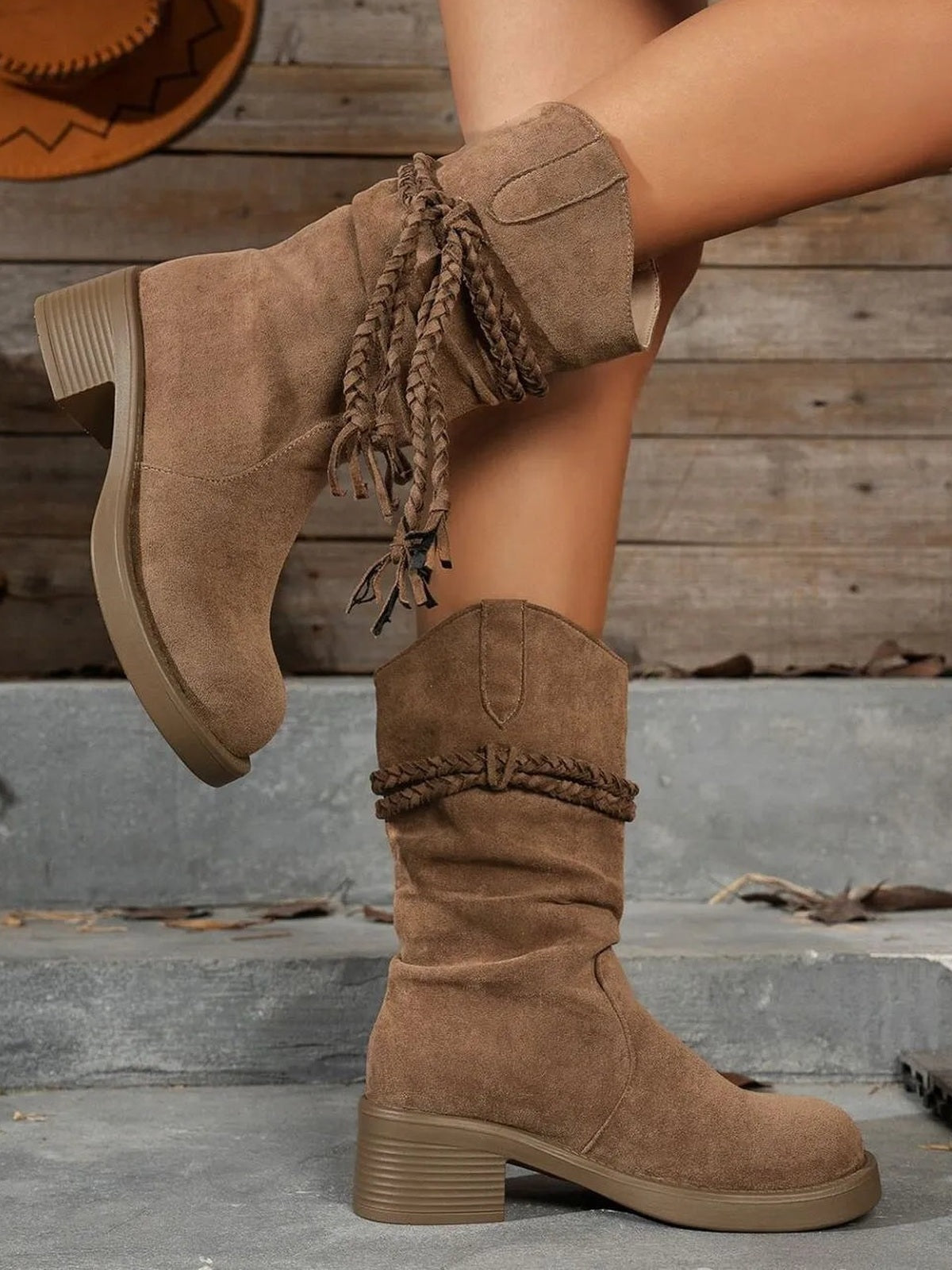 A model showcases brown round-toe boots with mid-height block heels, slouchy shafts, stitched panels, and braided wraparound laces.