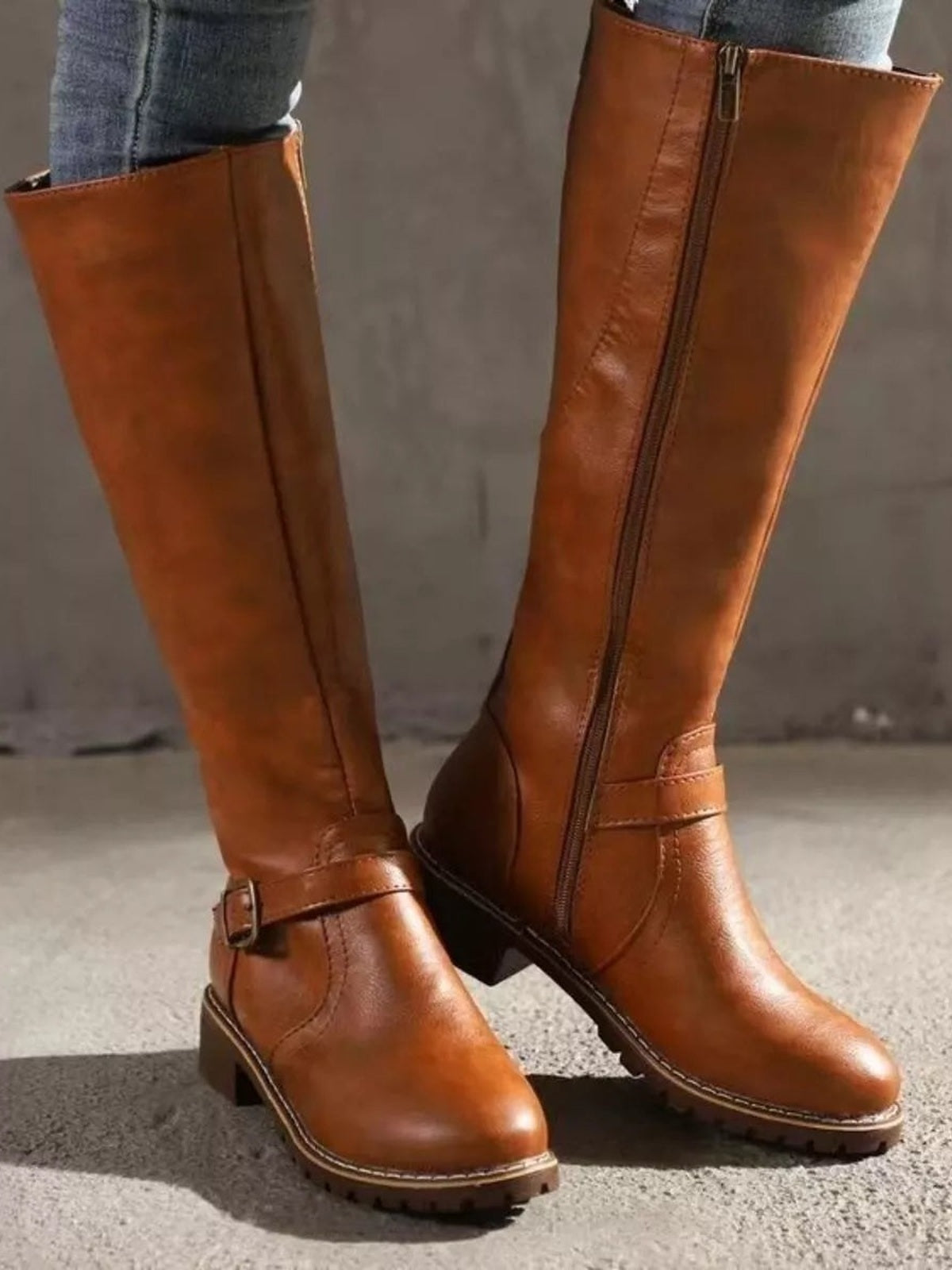 A model wears brown PU leather round-toe block-heel boots with tall shafts, side zippers, ankle straps, and stitched panel construction.