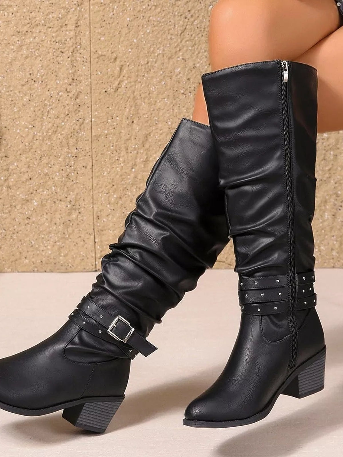 Black PU leather round-toe block-heel boots feature tall ruched shafts, side zippers, and buckled studded straps, shown on a model in a crossed-leg pose.