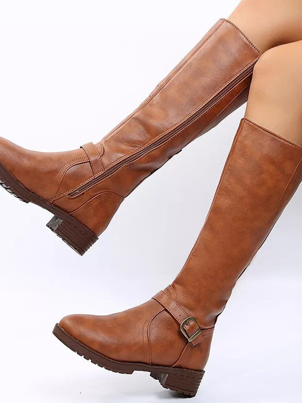 A model poses in brown PU leather round-toe boots with tall shafts, side zippers, buckled straps, and low block heels.