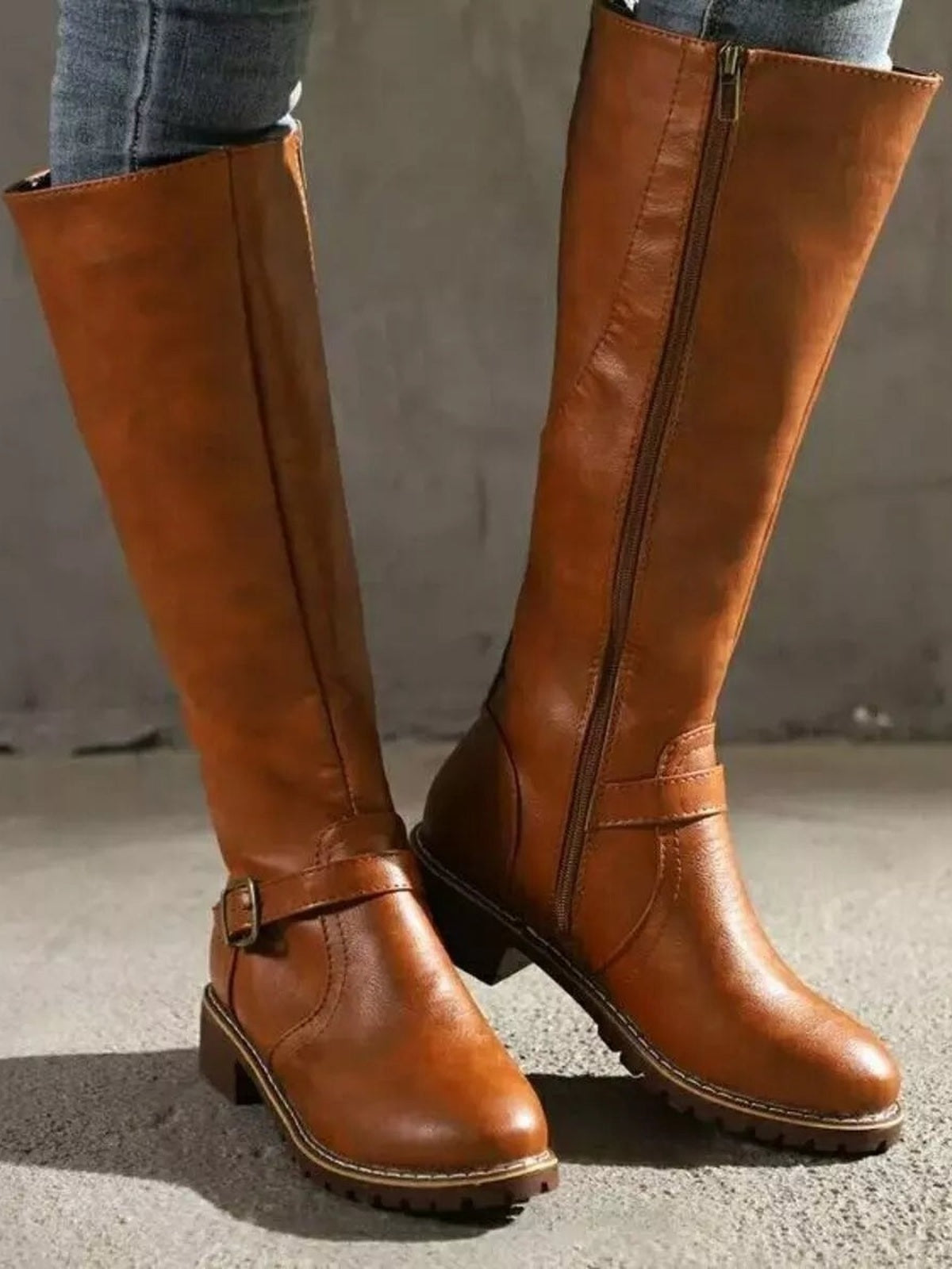 A model stands in tan PU leather tall boots with round toes, low block heels, side buckle straps, full-length zippers, and rugged rubber soles.