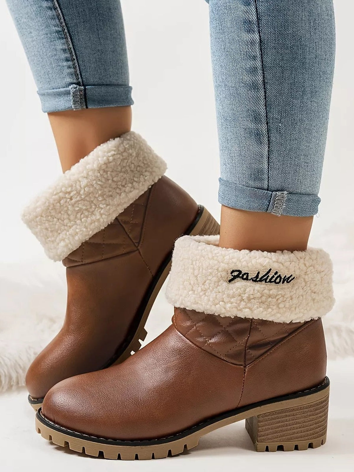 A model wears brown PU leather round-toe block-heel boots with quilted ankle panels, plush cream fluff cuffs, and rugged rubber soles.
