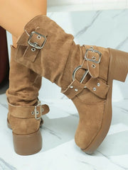 Camel suede boots with round toes, low block heels, and decorative silver-tone buckle straps, shown worn with one foot raised.