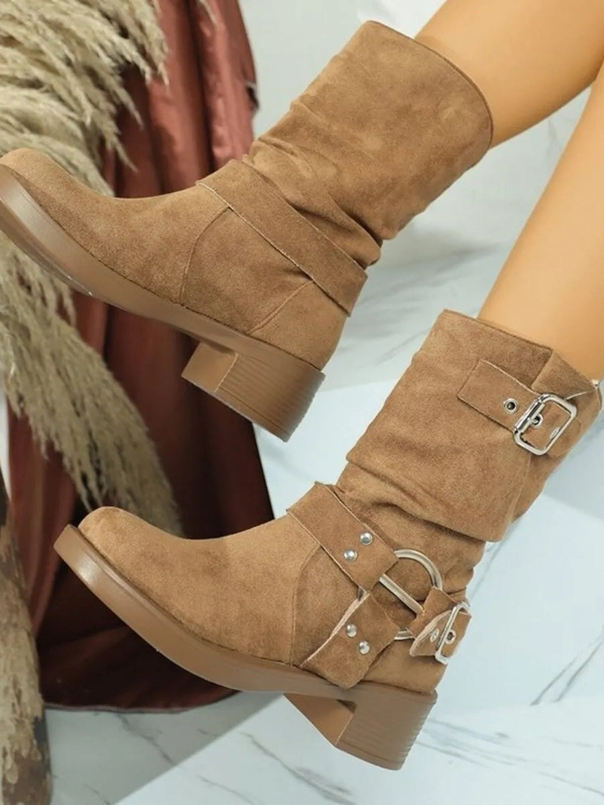 Model displays tan suede round-toe block-heel boots with slouchy shafts, layered straps, and silver buckle hardware.