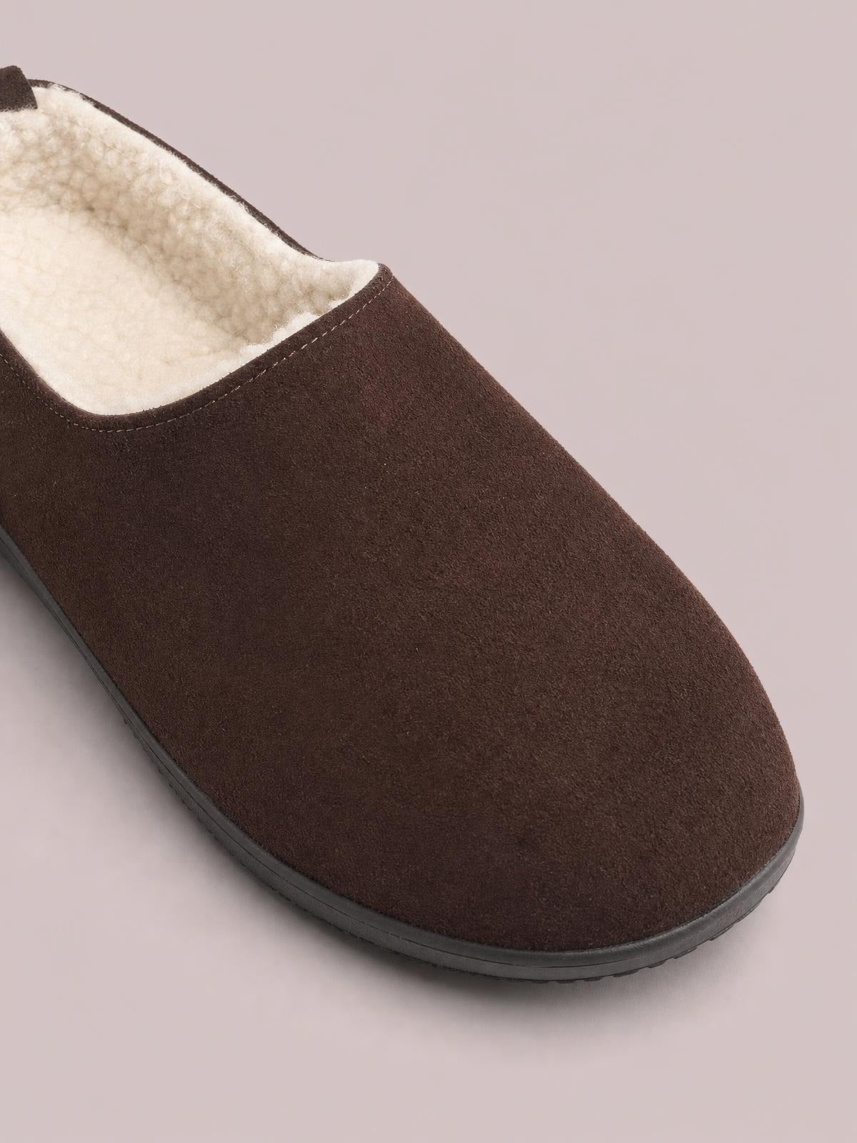 Brown suede round-toe flat slipper with a soft cream shearling-style lining, clean stitched edge, and a low black rubber sole.