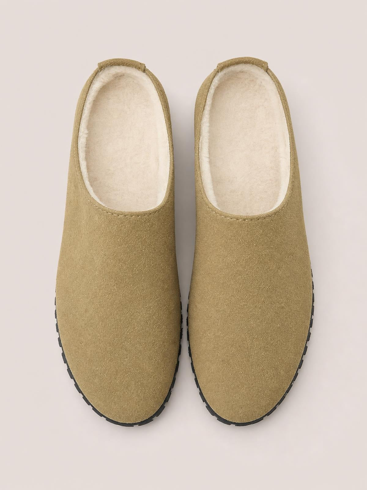 Pair of tan suede round-toe flat slippers with open backs, soft cream lining, stitched toplines, and black rubber soles.