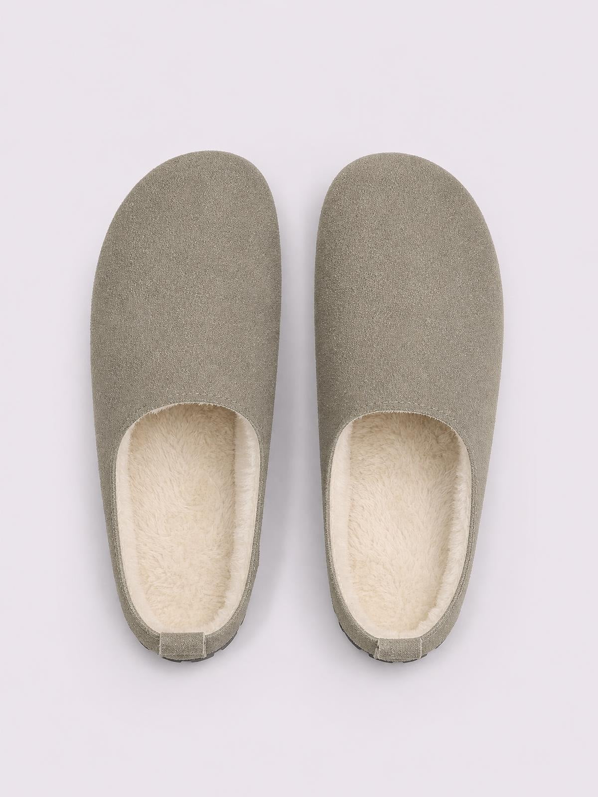 Pair of taupe suede round toe flats slippers shown from above, featuring a slip-on silhouette, plush cream lining, and low rubber soles.