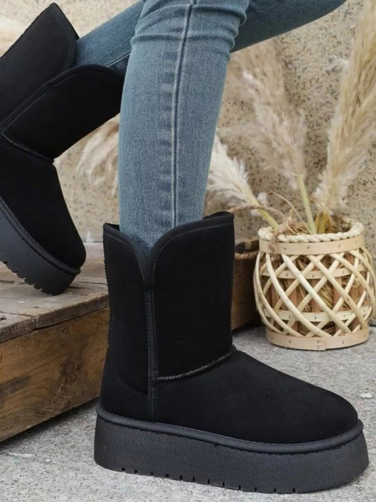 A model poses in blue jeans wearing black round toe platform boots with tall shafts, stitched panels, a smooth upper, and thick rubber soles.