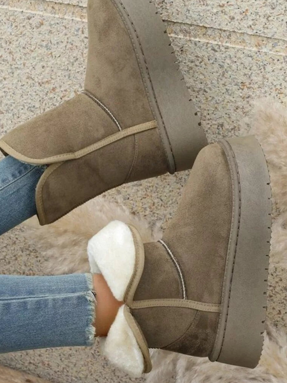 A model wears taupe round-toe platform boots with stitched panels, plush lining, and thick lugged rubber soles, paired with blue jeans.