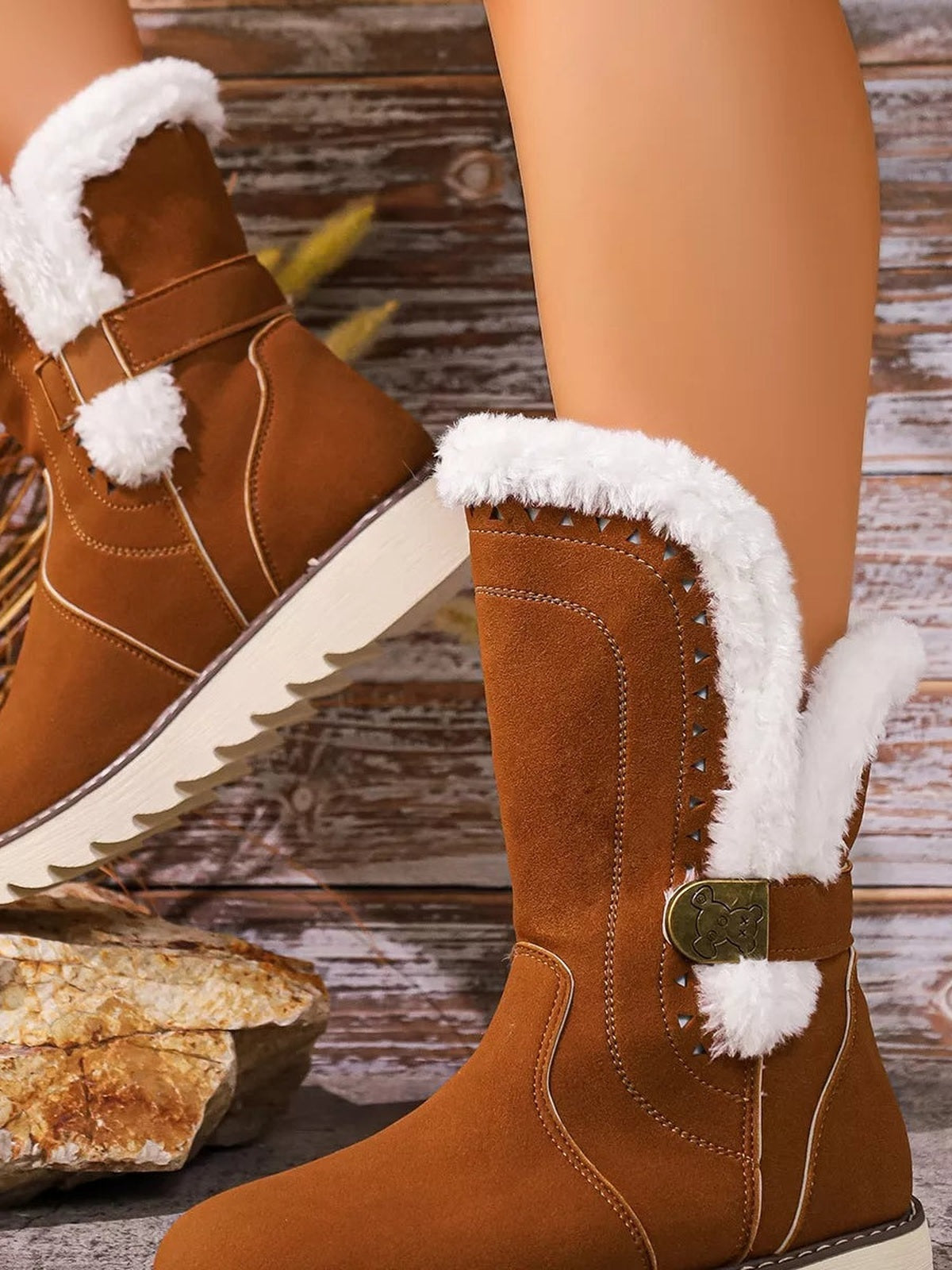 A model wears brown round-toe platform boots with white fluffy trim, stitched panels, decorative straps, and thick rubber soles in a relaxed crossed-leg pose.