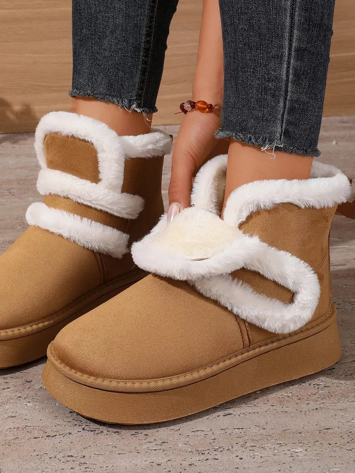 Model wears tan suede round toe platform boots with thick flat rubber soles, plush white fluff trim, and contrasting wraparound bands.