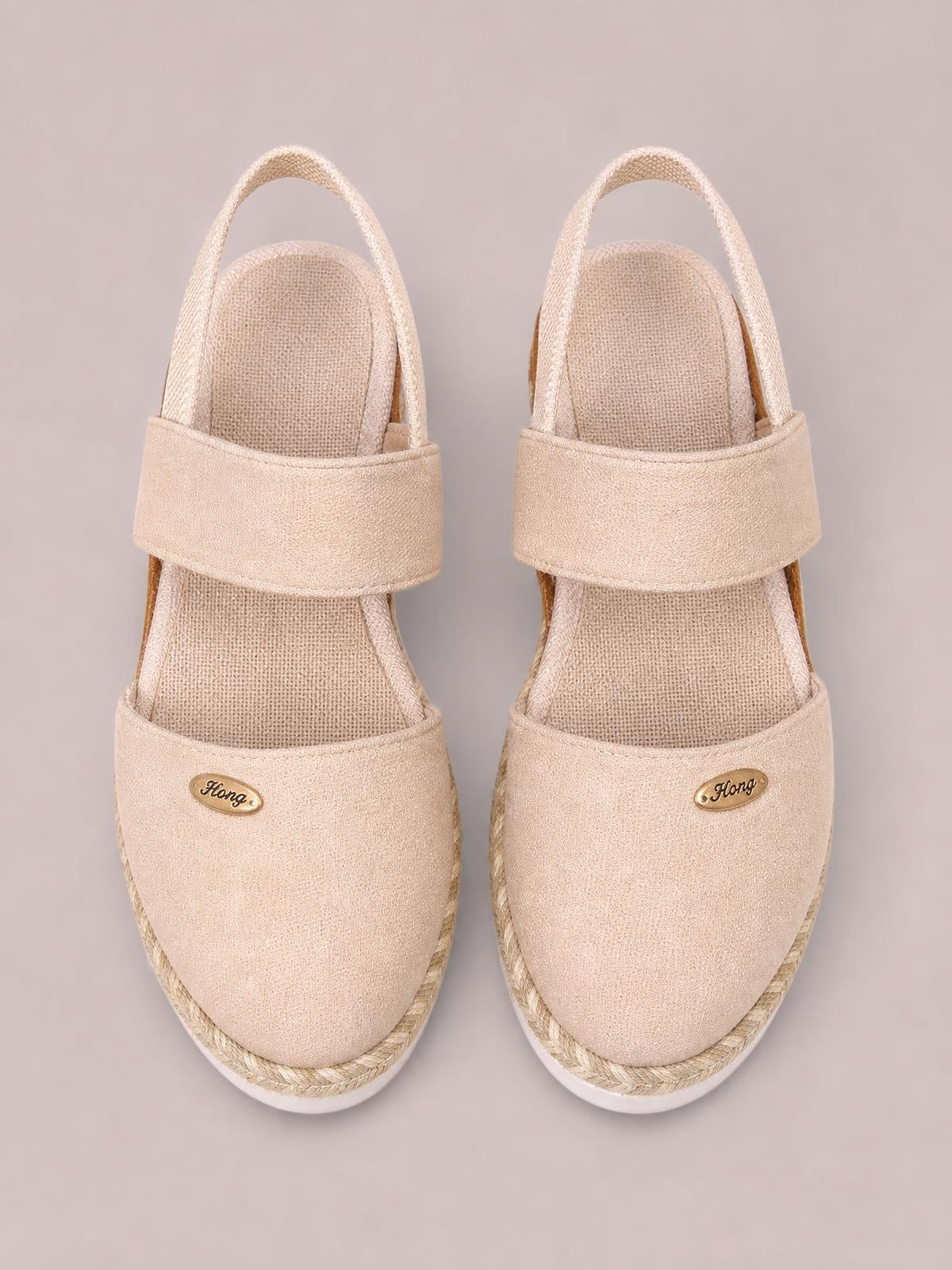 Beige canvas round toe wedge sandals with wide crossover straps, slingback ankle straps, rope-trimmed midsoles, and white rubber soles.
