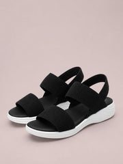 Black rubber open-toe low heel sandals feature wide textured crossover straps, ankle straps, and contrasting white molded soles.