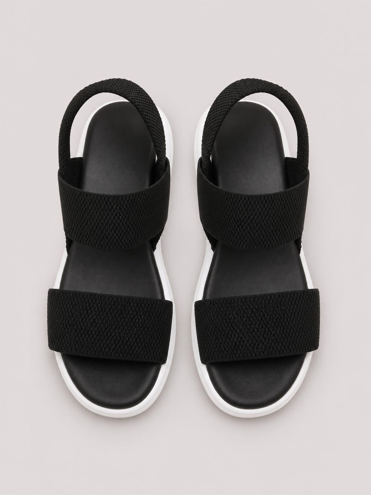 Pair of black open toe low heel sandals with textured wide straps, ankle loops, cushioned footbeds, and contrasting white rubber soles.