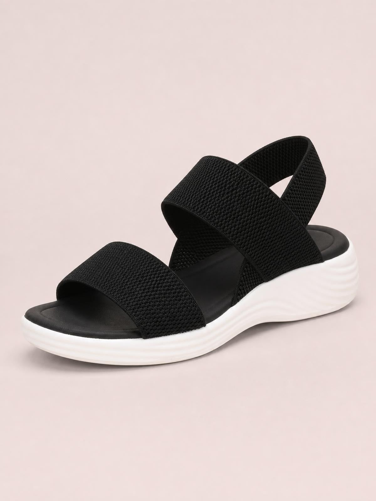 Black open-toe low-heel sandals with wide textured crossover straps, an adjustable heel strap, and a thick white platform sole.