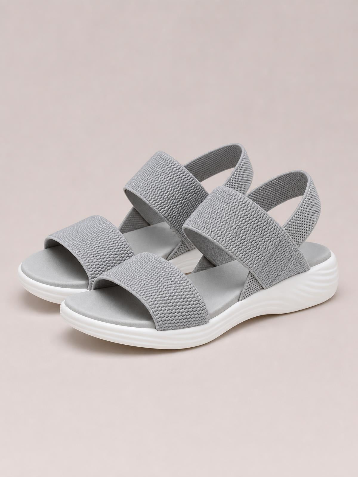 Gray rubber open-toe low-heel sandals feature wide textured straps, adjustable-looking heel bands, cushioned footbeds, and thick white soles.