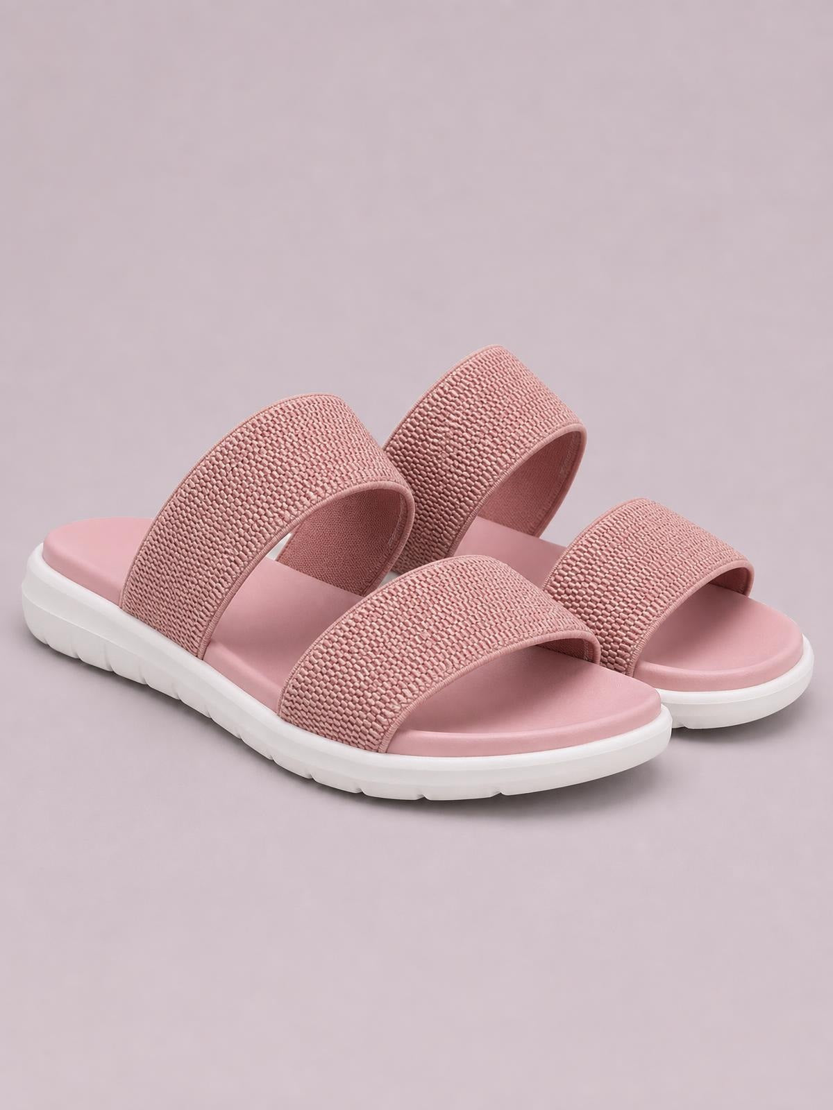 Pink open-toe low-heel sandals feature wide textured crossover straps, cushioned footbeds, and chunky white rubber soles.
