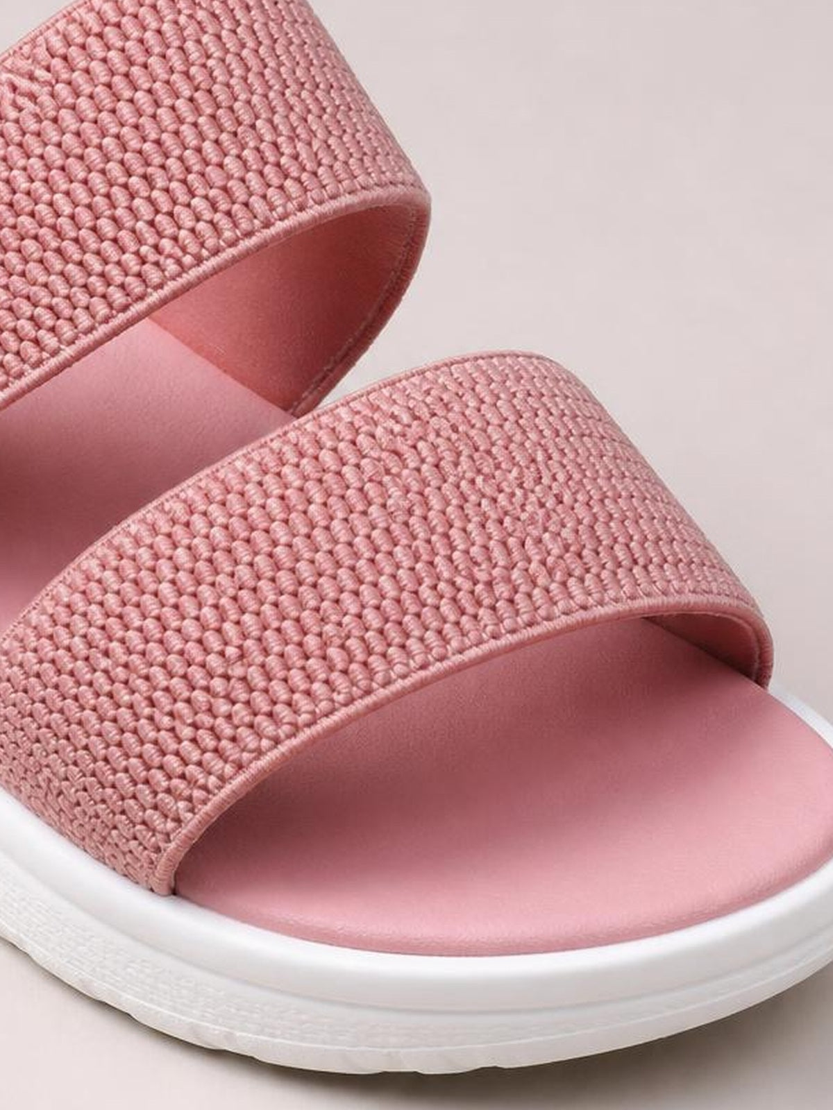 Close-up of pink rubber open toe low heel sandals with wide textured woven-look straps, smooth footbeds, and thick white soles.