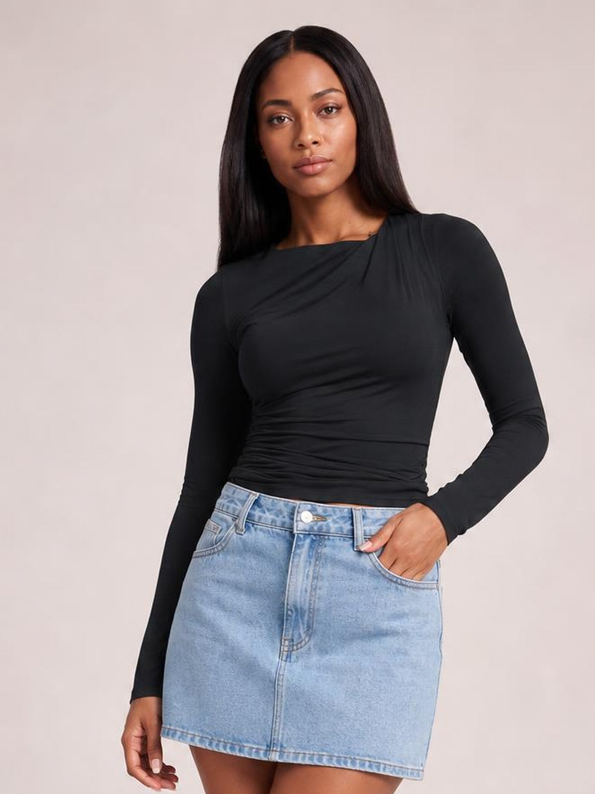 A model poses in a fitted black ruched asymmetrical-neck long-sleeve T-shirt with a sleek silhouette, one hand resting in her denim skirt pocket.