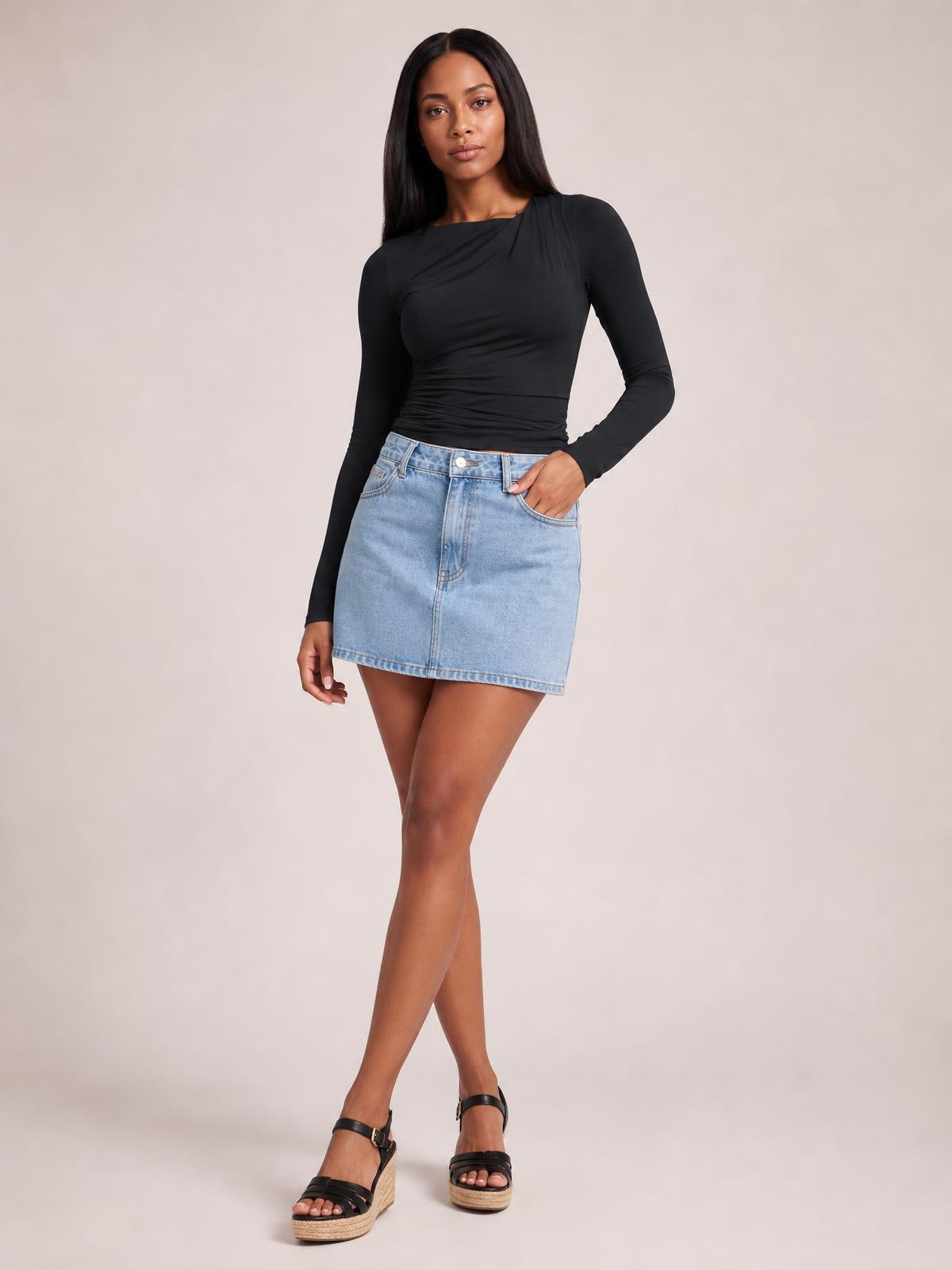 Model wears a fitted black ruched asymmetrical-neck long-sleeve T-shirt with a smooth silhouette, posed with one hand in her denim skirt pocket.