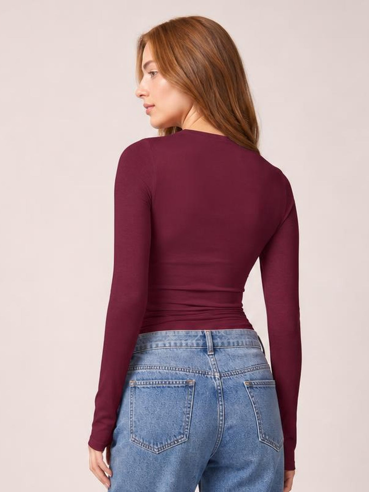 Model shown from behind wearing a burgundy long sleeve T-shirt with a fitted silhouette and visible horizontal ruching through the waist.