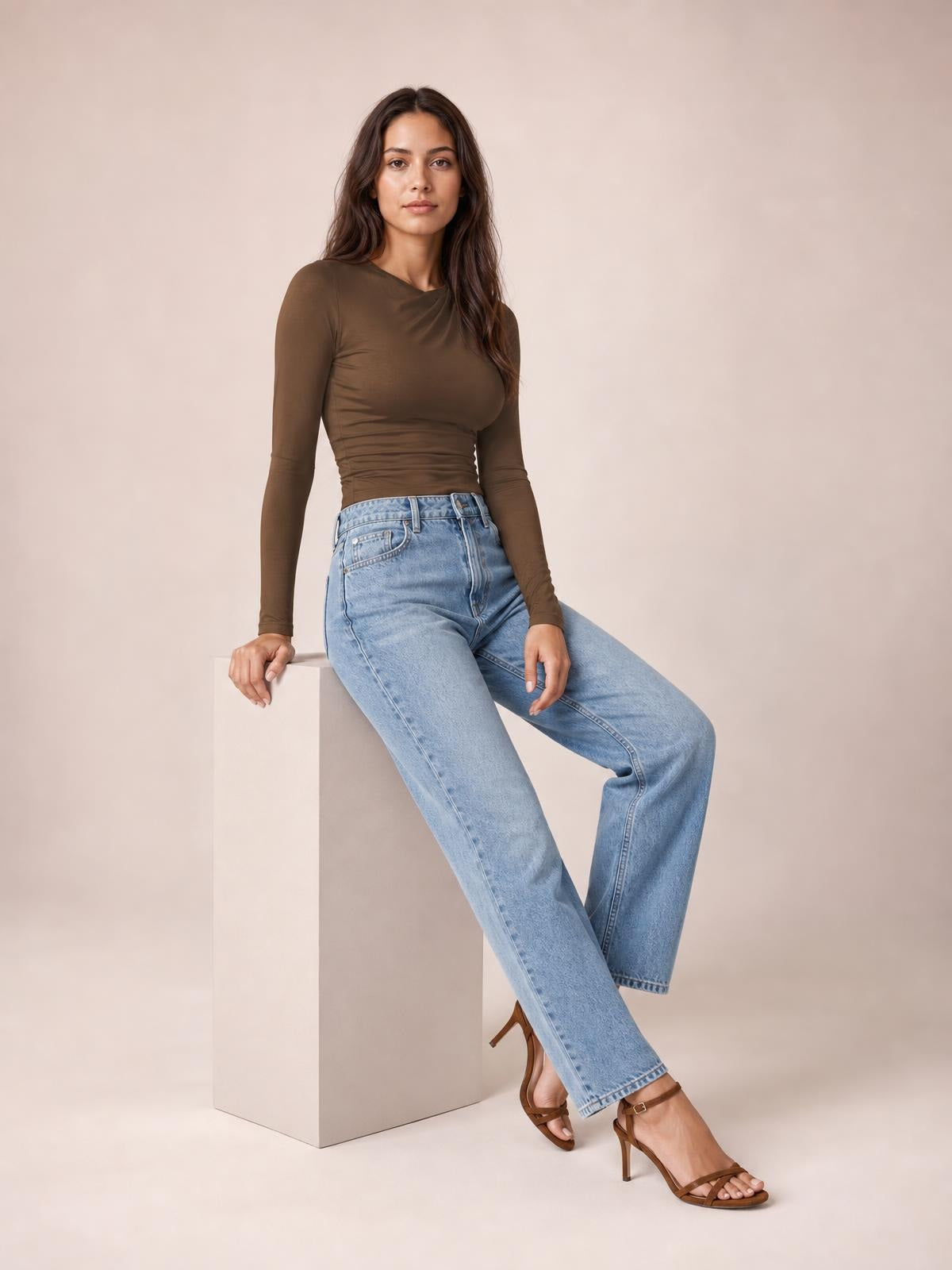 Model seated in a modern chic brown ruched asymmetrical neck long sleeve T-shirt with a fitted silhouette and gathered construction.