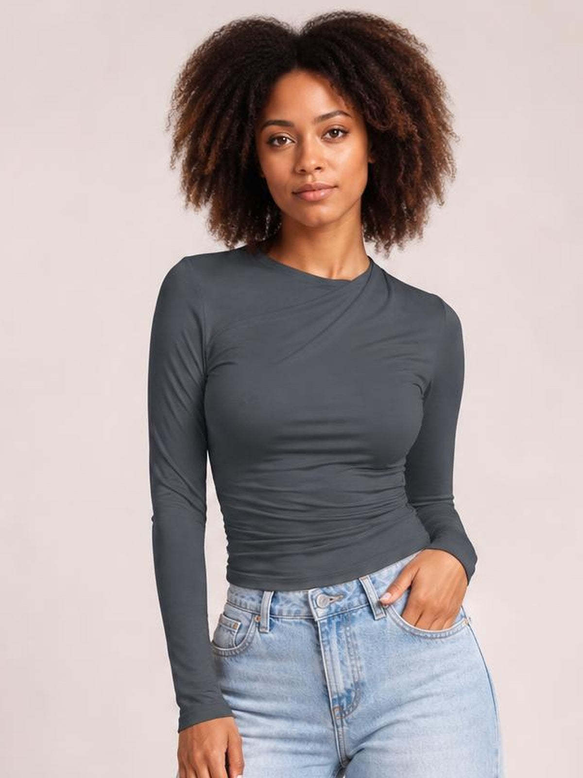 Model wearing a charcoal gray ruched asymmetrical neck long sleeve T-shirt with a fitted silhouette and gathered construction at the waist.