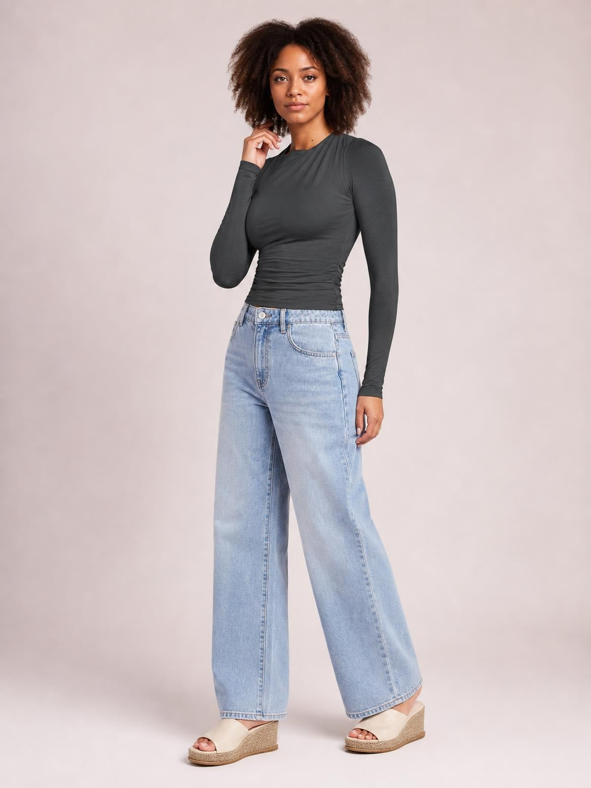 Model poses in a charcoal ruched asymmetrical-neck long-sleeve T-shirt with a fitted silhouette and gathered waist.