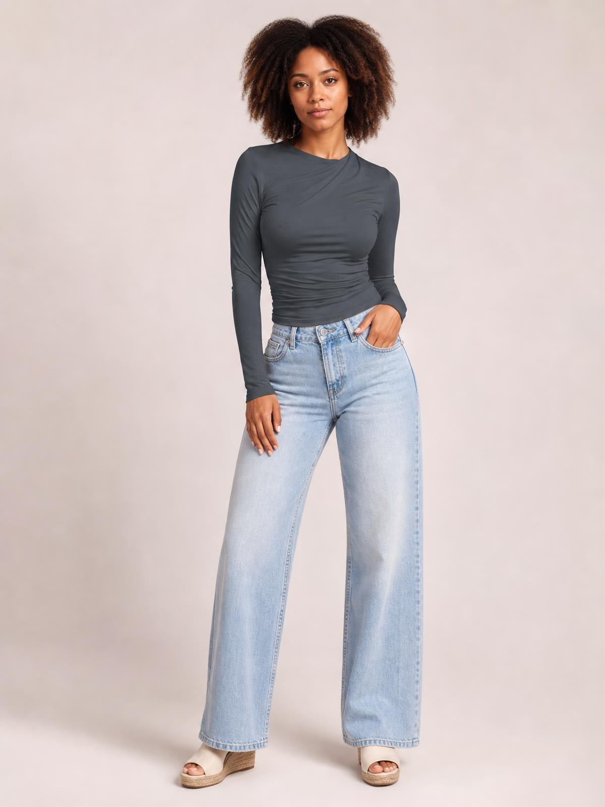 A model poses in a charcoal Ruched Asymmetrical Neck Long Sleeve T-Shirt with a fitted silhouette, gathered waist, and long sleeves, paired with wide-leg jeans.
