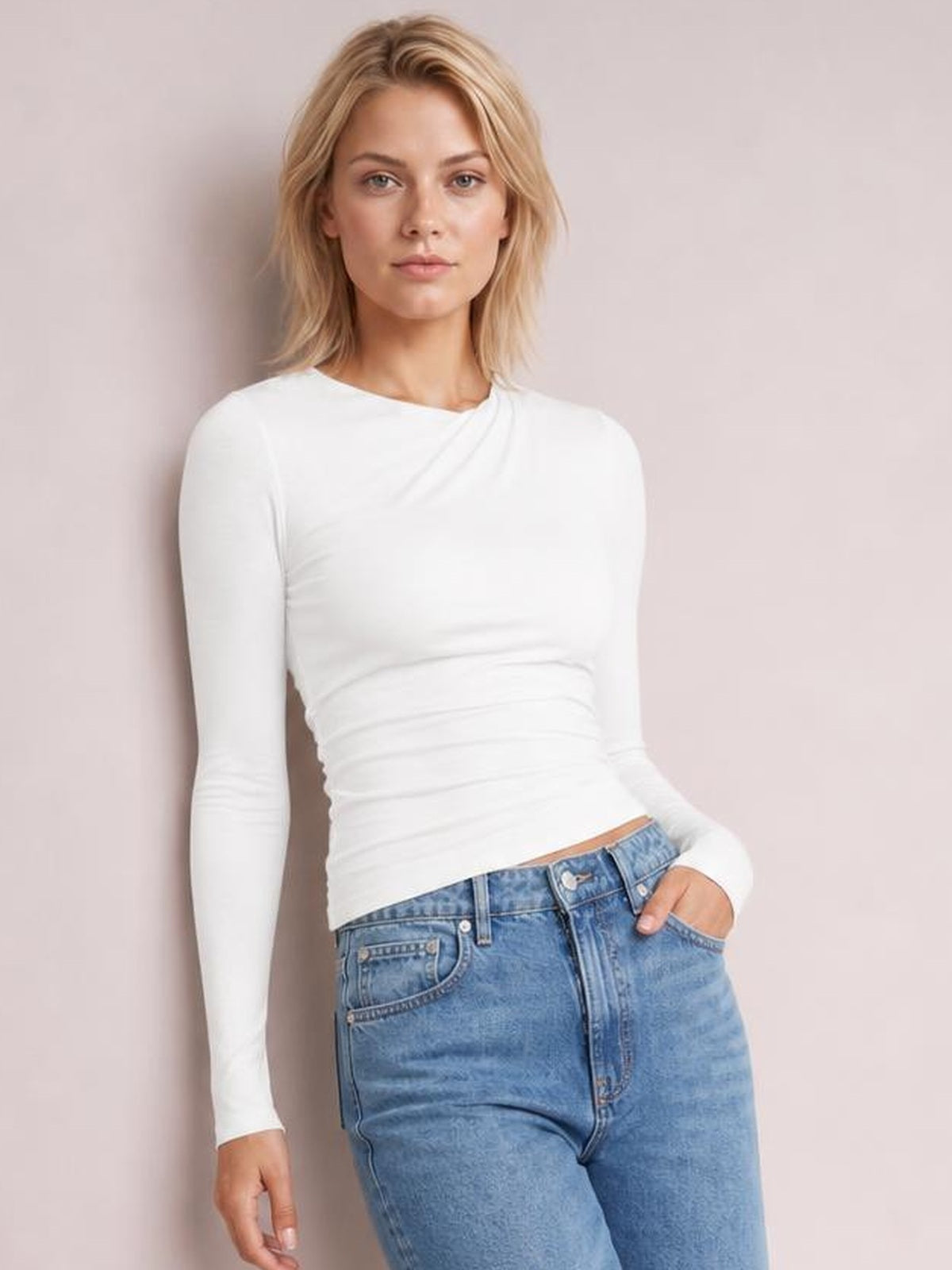 Model wearing a white ruched asymmetrical neck long sleeve T-shirt with a fitted silhouette, gathered waist, and slight stretch.