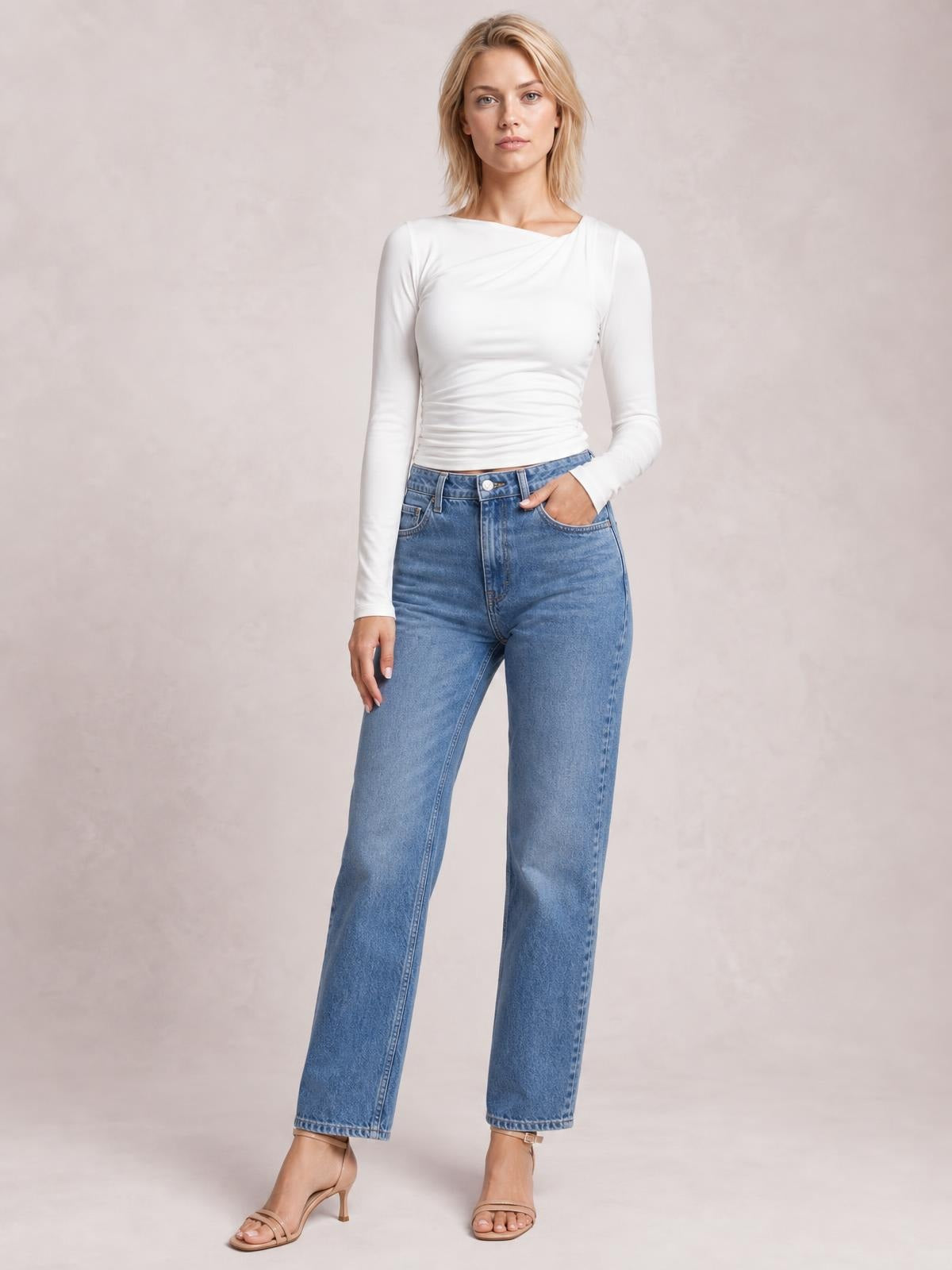 Model stands in a white ruched asymmetrical-neck long-sleeve T-shirt with a fitted silhouette, paired with straight-leg jeans and one hand in a pocket.