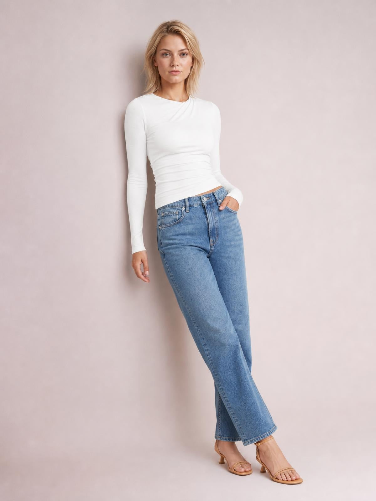 Model wears a white ruched asymmetrical-neck long-sleeve T-shirt with a fitted silhouette, standing with one hand in her jeans pocket.