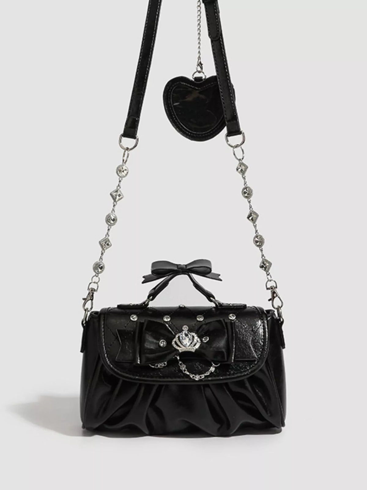 Small black PU leather crossbody bag with a ruched silhouette, bow details, flap closure, decorative chain strap, and silver-tone hardware.