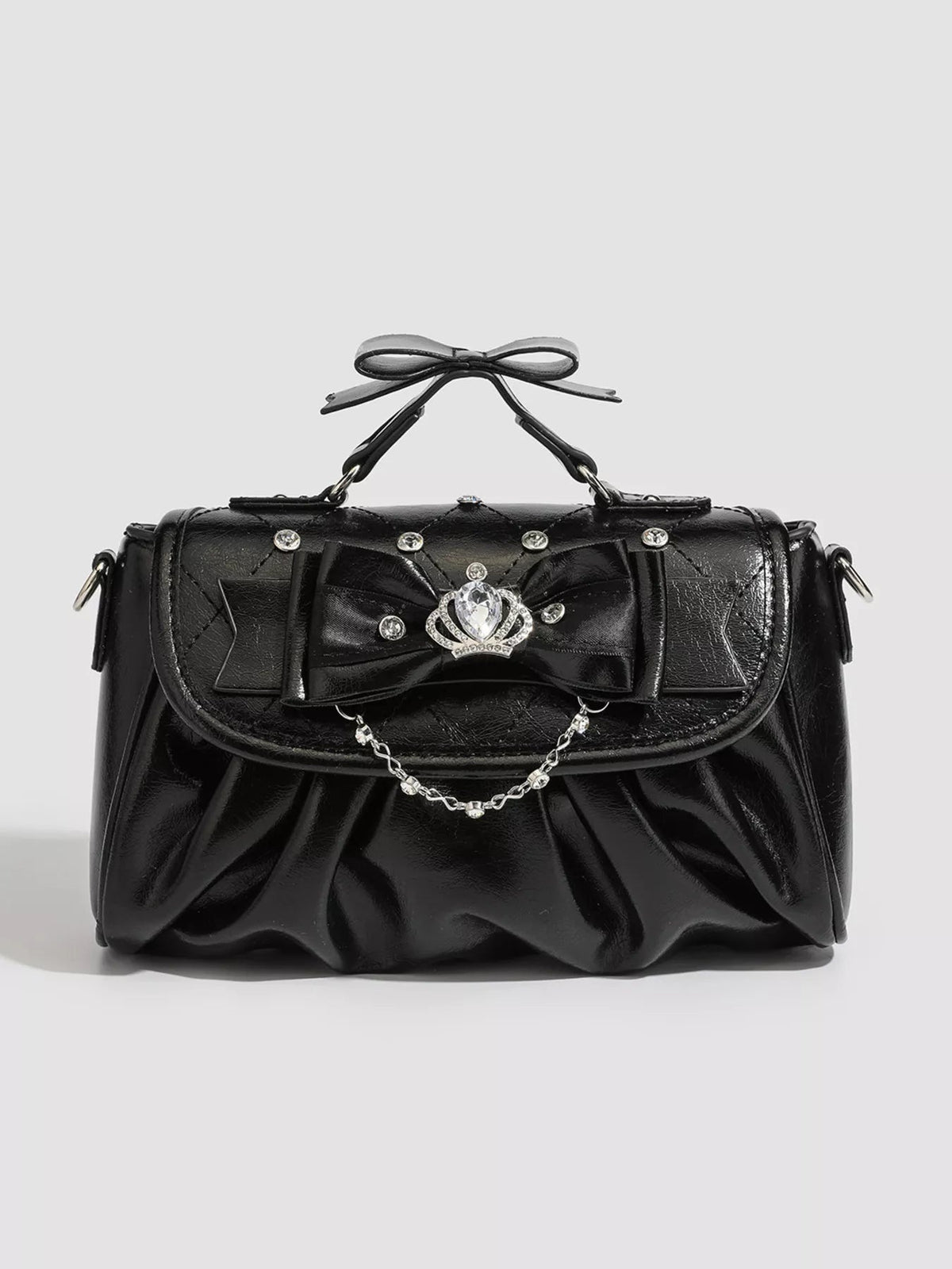 Small black PU leather crossbody bag with a ruched silhouette, structured top handle, oversized bow, rhinestone embellishments, and a delicate chain accent.