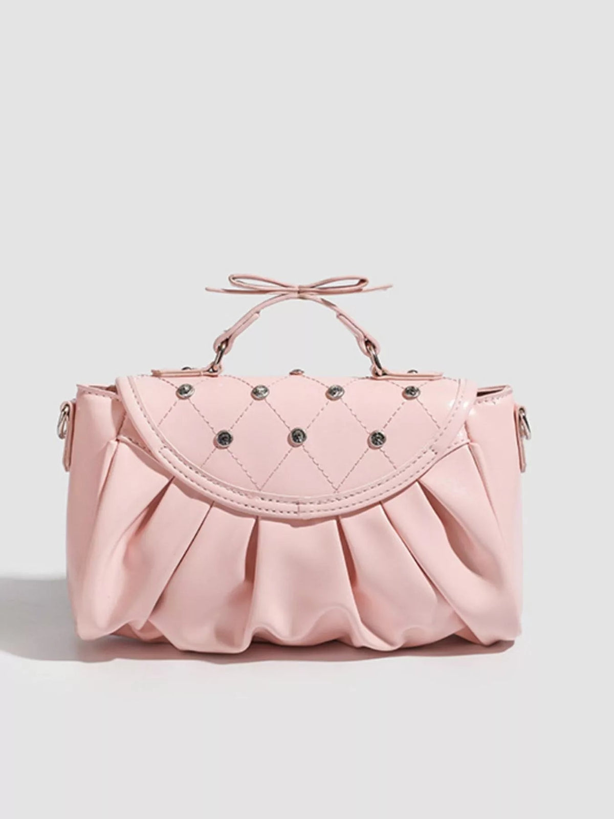 Small pink PU leather crossbody bag with a ruched bow top handle, quilted flap, stud accents, curved silhouette, and gathered pleat construction.