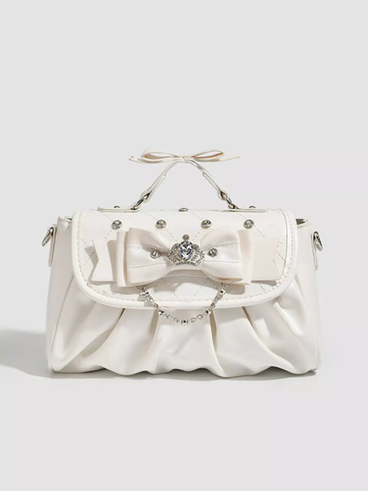 White small PU leather crossbody bag with a ruched, softly pleated silhouette, oversized bow, jeweled clasp, chain accent, and top handle.