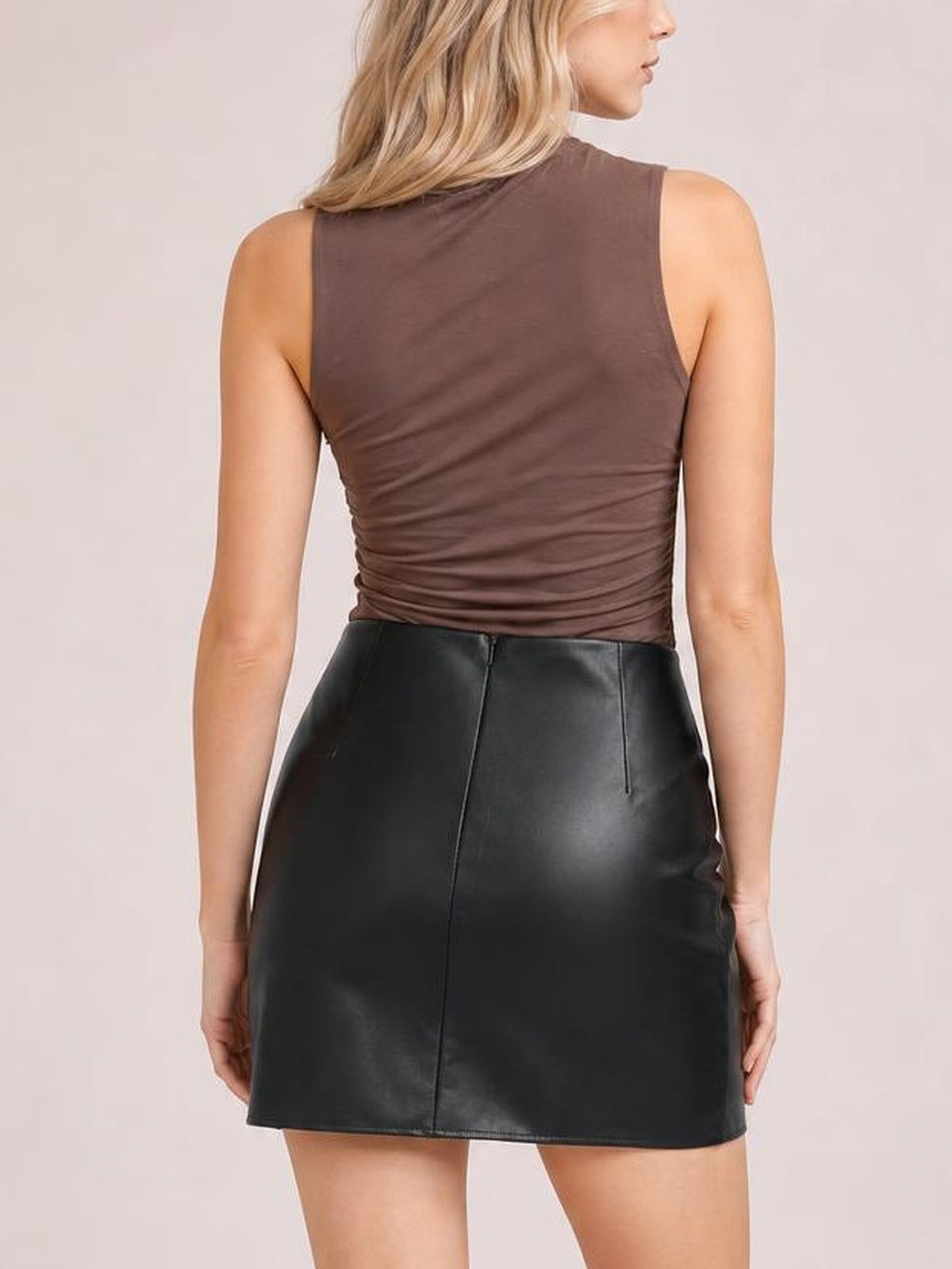 Model shown from the back wearing a black mini skirt with a smooth fitted silhouette, center-back seam, and visible waistband zipper.