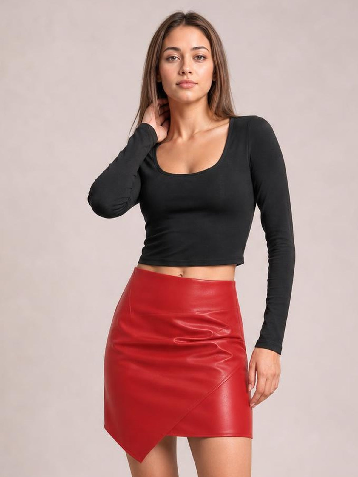 A model poses with one hand near her neck, wearing a red ruched mini skirt with a fitted silhouette, glossy finish, and asymmetrical pointed hem.