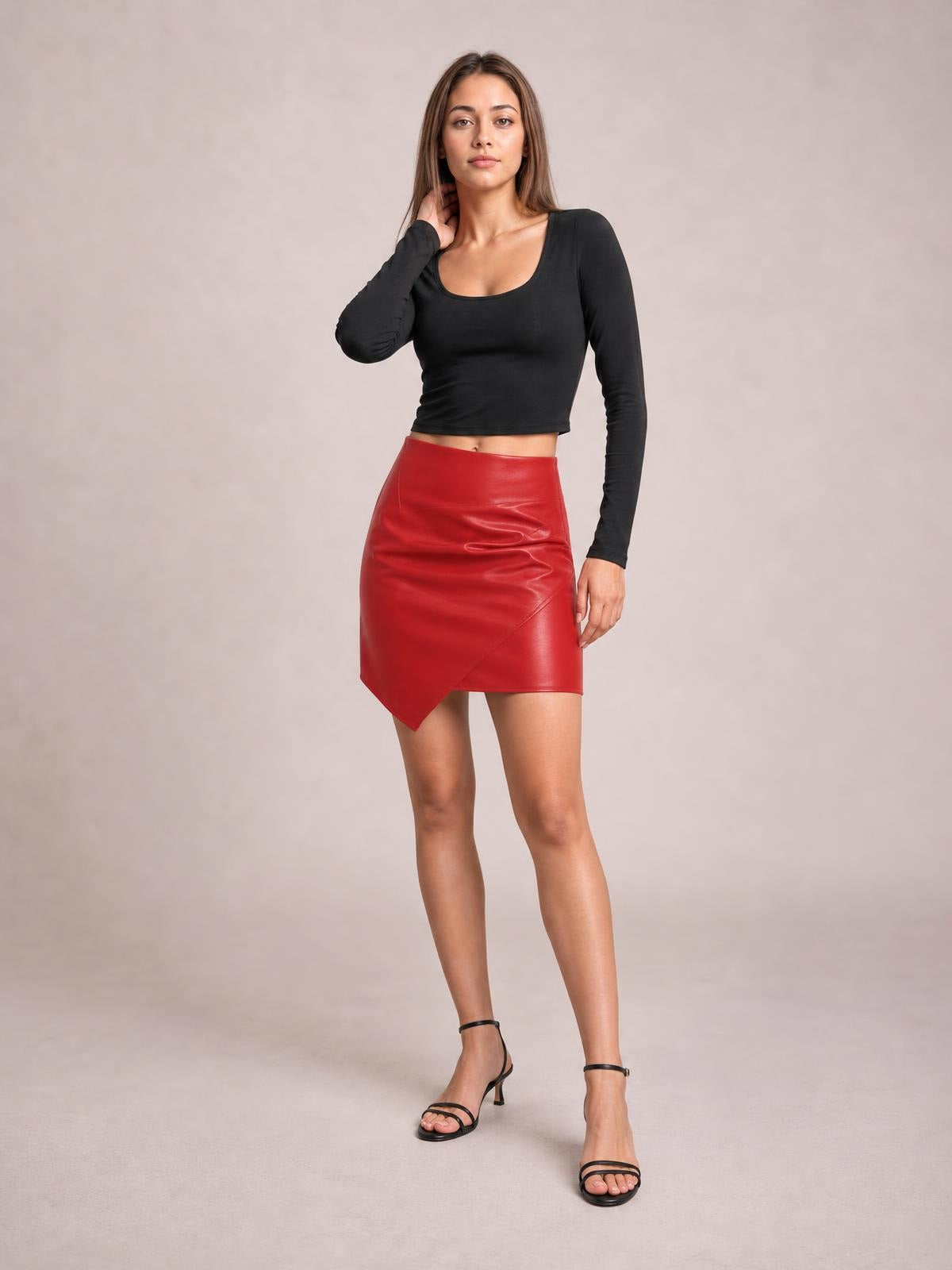 Model poses in a red ruched mini skirt with a fitted silhouette and asymmetrical hem, styled with a black long-sleeve scoop-neck top.