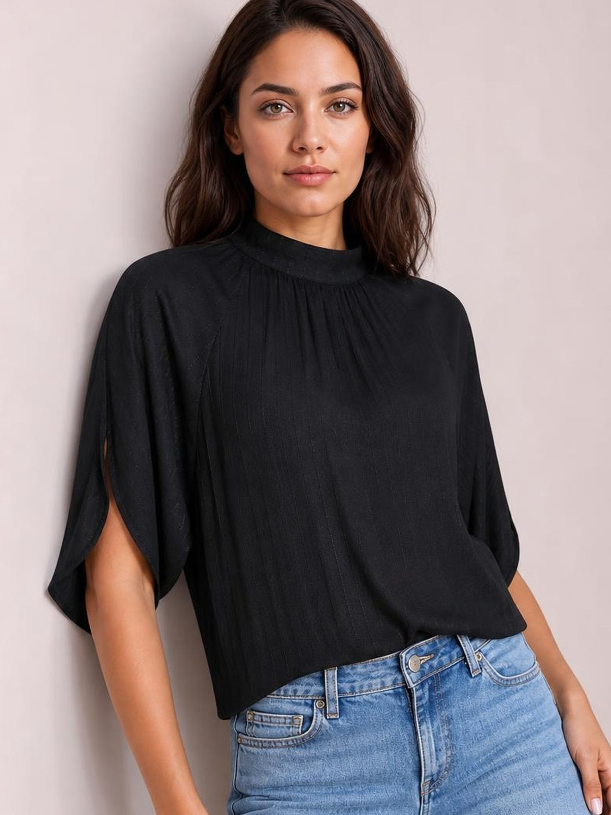 A model poses in a black ruched mock neck blouse with gathered detailing, loose half sleeves, and a relaxed straight silhouette.