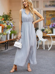 Model wears a gray ruched notched sleeveless midi dress with a defined waist and fluid, softly draped skirt, posing with one hand on her hip.