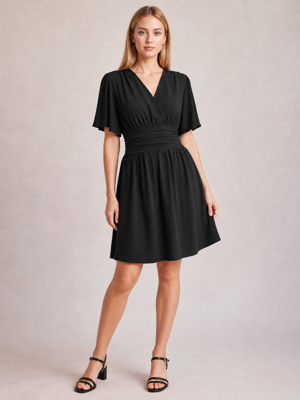 Model poses in a black ruched surplice short sleeve dress with a defined waistband, gathered flared skirt, and above-knee hem.